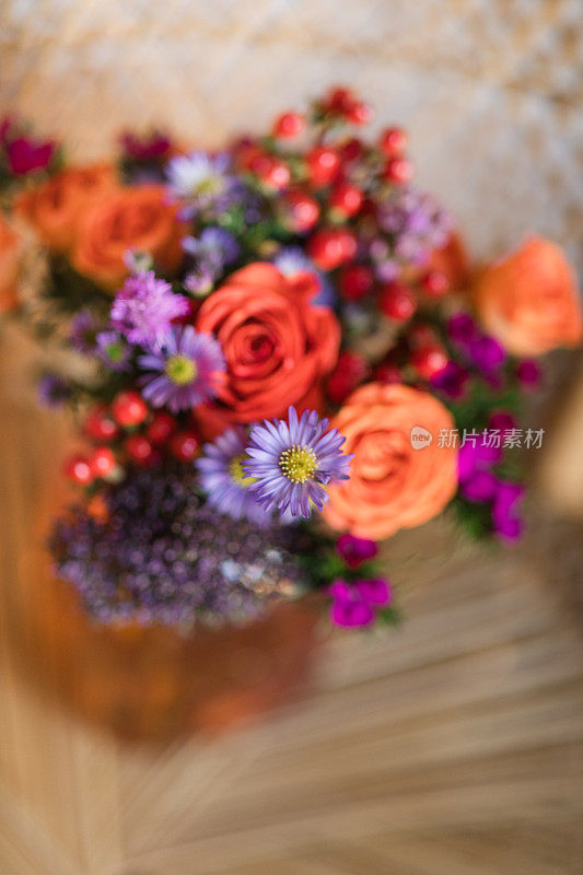 A Colorful Summer Floral Arrangement of Coral Roses, Purple Daisies, Red Berries & Other Flowers in an Orange Mason Jar Glass Vase Sitting on a Boho Vintage Rattan Peacock Chair in South Florida in the Summer of 2023